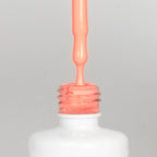 Nahaufnahme einer offenen Longlife UV-Lack Brazil Flasche. Die Farbe ist ein helles Orange mit Rosa-Stich. Der UV-Nagellack tropft am Pinsel herunter.