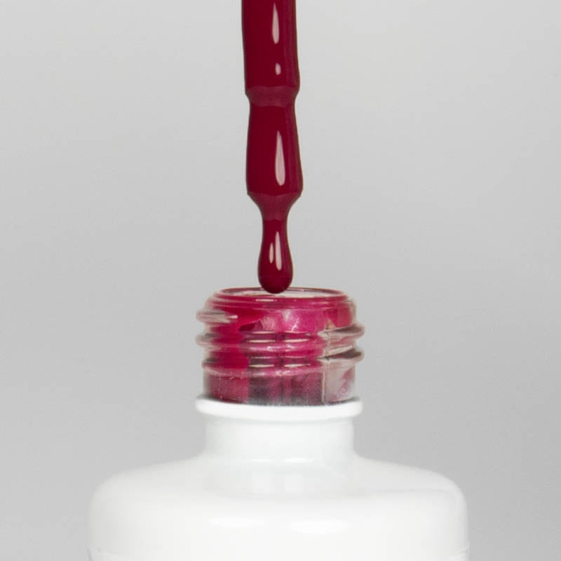 Nahaufnahme einer offenen Longlife UV-Lack Dragon Flasche. Die Farbe ist ein dunkles Pink. Der UV-Nagellack tropft am Pinsel herunter.