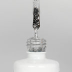 Nahaufnahme einer offenen Longlife UV-Lack Egg Shell Shiny Silver Flasche. Die Farbe ist transparent mit silbernen Partikeln. Der UV-Nagellack tropft am Pinsel herunter.
