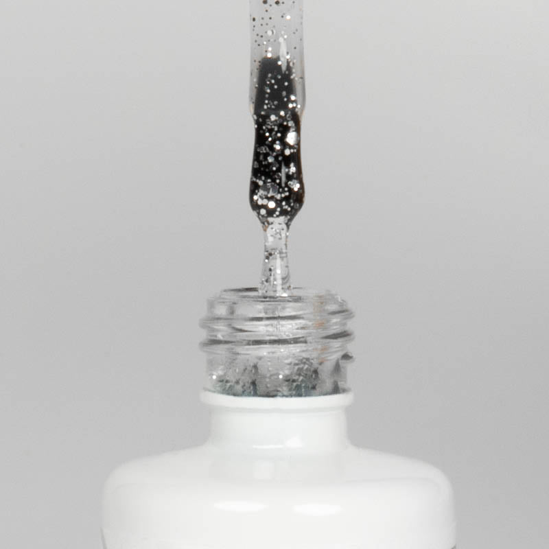 Nahaufnahme einer offenen Longlife UV-Lack Egg Shell Shiny Silver Flasche. Die Farbe ist transparent mit silbernen Partikeln. Der UV-Nagellack tropft am Pinsel herunter.