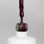 Nahaufnahme einer offenen Longlife UV-Lack Gipsy Flasche. Die Farbe ist ein dunkles Violett mit Rot-Stich mit niedriger Sättigung. Der UV-Nagellack tropft am Pinsel herunter.