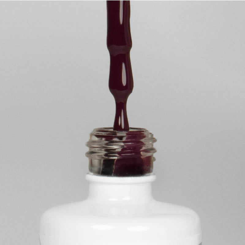 Nahaufnahme einer offenen Longlife UV-Lack Gipsy Flasche. Die Farbe ist ein dunkles Violett mit Rot-Stich mit niedriger Sättigung. Der UV-Nagellack tropft am Pinsel herunter.