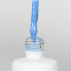 Nahaufnahme einer offenen Longlife UV-Lack Intensive Blue Flasche. Die Farbe ist ein helles Blau mit hoher Sättigung. Der UV-Nagellack tropft am Pinsel herunter.