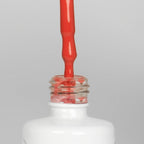 Nahaufnahme einer offenen Longlife UV-Lack Koi Flasche. Die Farbe ist ein helles Orange-Rot mit hoher Sättigung. Der UV-Nagellack tropft am Pinsel herunter.
