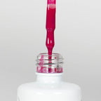 Nahaufnahme einer offenen Longlife UV-Lack Magenta Flasche. Die Farbe ist ein kräftiges Pink. Der UV-Nagellack tropft am Pinsel herunter.