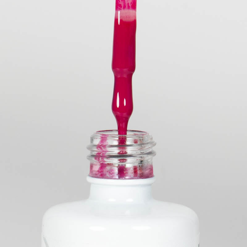 Nahaufnahme einer offenen Longlife UV-Lack Magenta Flasche. Die Farbe ist ein kräftiges Pink. Der UV-Nagellack tropft am Pinsel herunter.