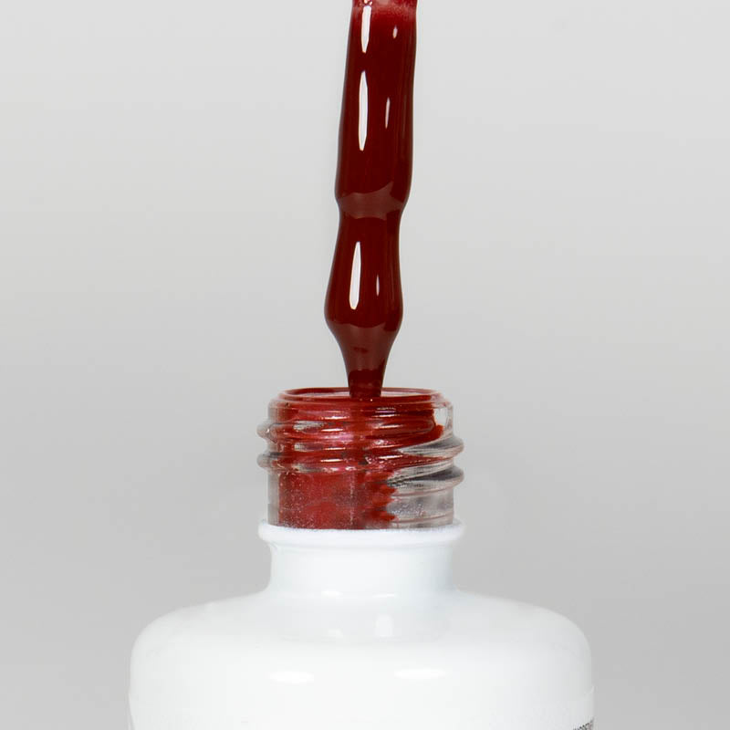 Nahaufnahme einer offenen Longlife UV-Lack Marsala Flasche. Die Farbe ist ein dunkles Rot mit Braun-Stich. Der UV-Nagellack tropft am Pinsel herunter.