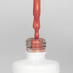 Nahaufnahme einer offenen Longlife UV-Lack Metallic Salmon Gold Flasche. Die Farbe ist ein Lachs-Orange mit goldenem Metallic_Effekt. Der UV-Lack tropft am Pinsel herunter.