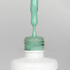 Nahaufnahme einer offenen Longlife UV-Lack Mint Flasche. Die Farbe ist ein helles Grün mit hoher Sättigung. Der UV-Lack tropft am Pinsel herunter.