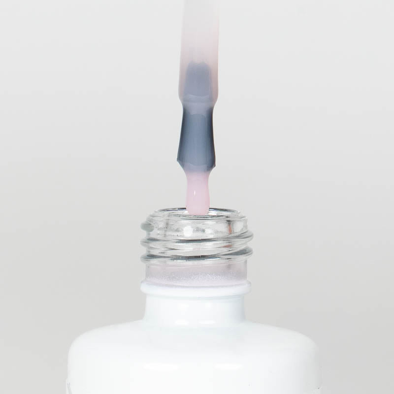 Nahaufnahme einer Longlife UV-Lack Top Gloss Milky Rose Flasche. Die Farbe ist ein leicht deckendes Rosa. Der UV-Lack tropft am Pinsel herunter.