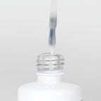 Nahaufnahme einer Longlife UV-Lack Top Gloss Milky White Flasche. Die Farbe ist ein leicht deckendes Weiß. Der UV-Lack tropft am Pinsel herunter.