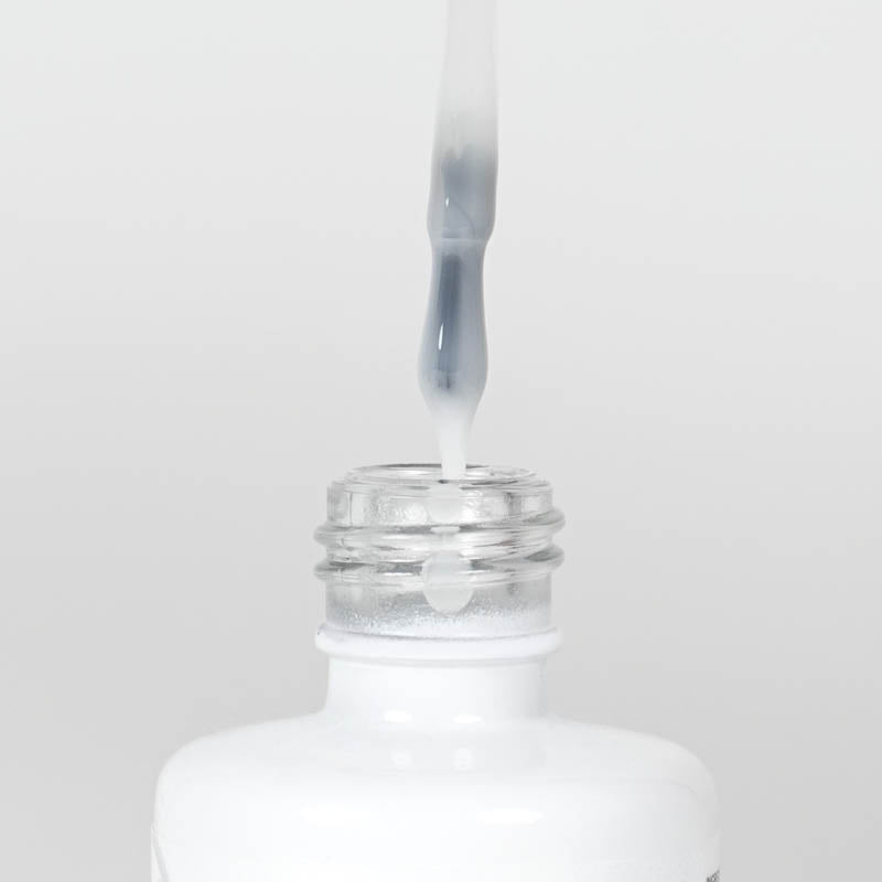 Nahaufnahme einer Longlife UV-Lack Top Gloss Milky White Flasche. Die Farbe ist ein leicht deckendes Weiß. Der UV-Lack tropft am Pinsel herunter.