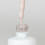 Nahaufnahme einer Longlife UV-Lack Flasche der Farbe Wellbeing. Die Farbe ist ein helles Nude. Der UV-Lack tropft am Pinsel herunter.