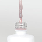 Nahaufnahme einer Longlife UV-Lack Rubber Base Cover Glitter Flasche. Die Farbe ist durchscheinend Rosa mit Glitzereffekt. Der UV-Lack tropft am Pinsel herunter.