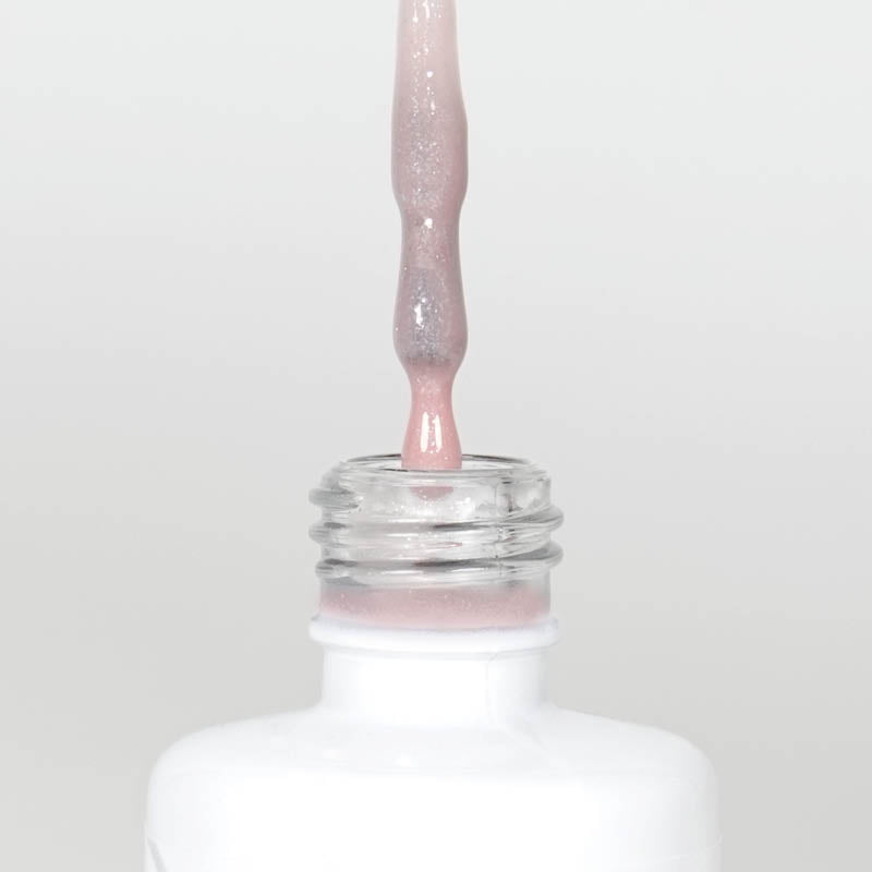 Nahaufnahme einer Longlife UV-Lack Rubber Base Cover Glitter Flasche. Die Farbe ist durchscheinend Rosa mit Glitzereffekt. Der UV-Lack tropft am Pinsel herunter.