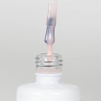 Nahaufnahme einer Longlife UV-Lack Rubber Base Cover Pearl Flasche. Die Farbe ist durchscheinend Nude-Rosé mit Perl-Effekt. Der UV-Lack tropft am Pinsel herunter.