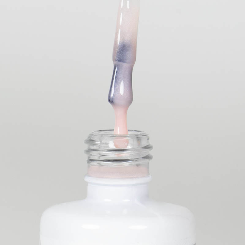 Nahaufnahme einer Longlife UV-Lack Rubber Base Cover Pearl Flasche. Die Farbe ist durchscheinend Nude-Rosé mit Perl-Effekt. Der UV-Lack tropft am Pinsel herunter.