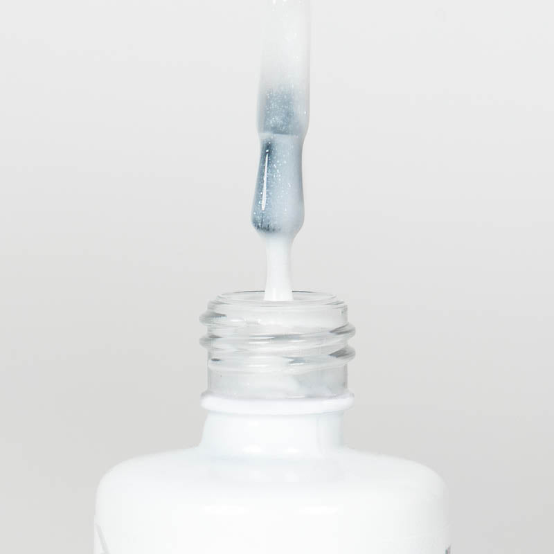 Nahaufnahme einer Longlife UV-Lack Rubber Base Cover Sparkling White Flasche. Die Farbe ist durchscheinend Weiß mit Glitzereffekt. Der UV-Lack tropft am Pinsel herunter.