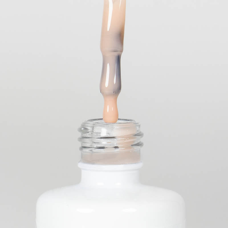 Nahaufnahme einer Longlife UV-Lack Rubber Base Cover Three Flasche. Die Farbe ist durchscheinend Nude mit Orange-Stich. Der UV-Lack tropft am Pinsel herunter.