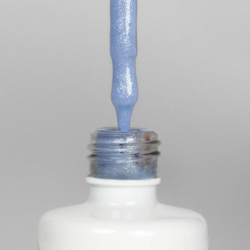 Nahaufnahme einer offenen Longlife UV-Lack Bella Emilia Flasche. Die Farbe ist ein helles Blau mit Glitzer-Effekt. Der UV-Nagellack tropft am Pinsel herunter.